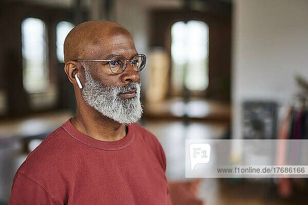 Mature man wearing eyeglasses listening music through in-ear headphones at home