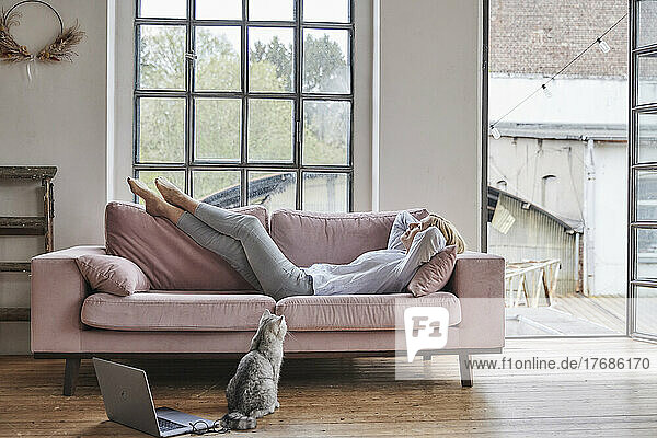Woman lying on sofa by window in living room at home