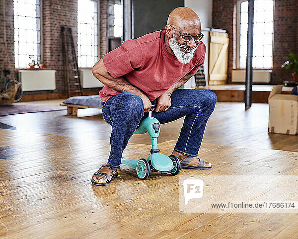 Smiling man riding small tricycle on floor at home