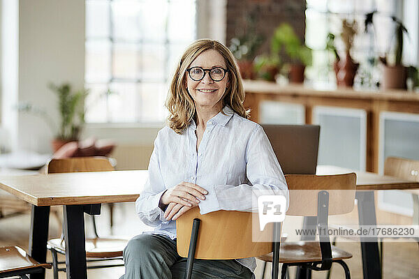Smiling woman wearing eyeglasses sitting on chair at home