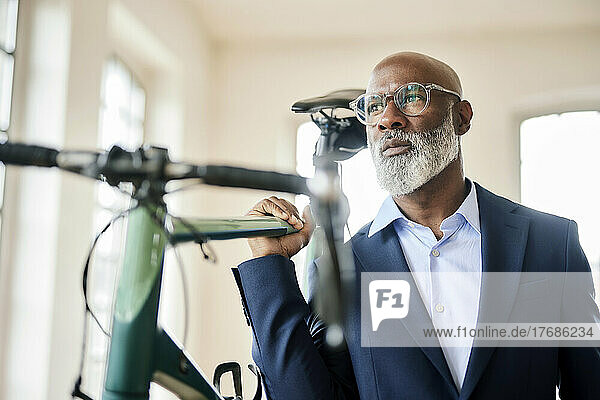 Thoughtful businessman carrying bicycle at home