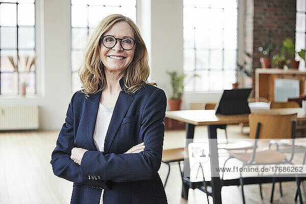 Happy businesswoman wearing eyeglasses standing with arms crossed at home