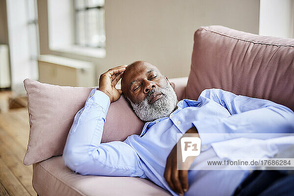 Bald businessman sleeping on sofa at home