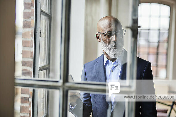 Thoughtful businessman seen through window at home
