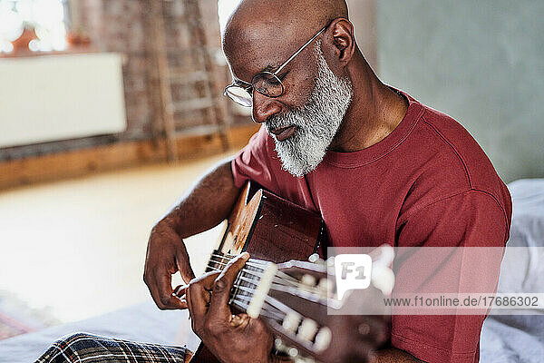 Man with eyeglasses playing guitar at home