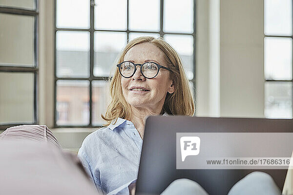 Thoughtful freelancer wearing eyeglasses sitting with laptop at home