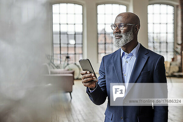 Thoughtful businessman with mobile phone at home