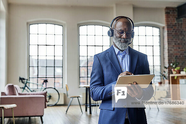 Smiling businessman with headset using tablet computer at home