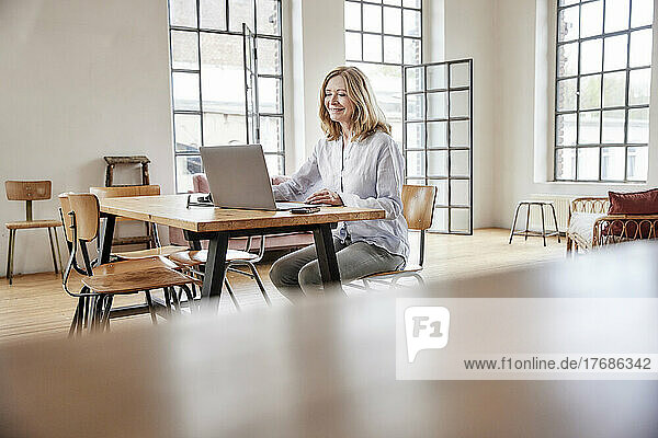 Smiling freelancer using laptop sitting at table in living room