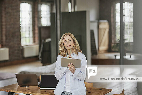 Thoughtful businesswoman with tablet PC leaning on table at home