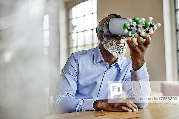Mature scientist with virtual reality simulator examining molecular model at home