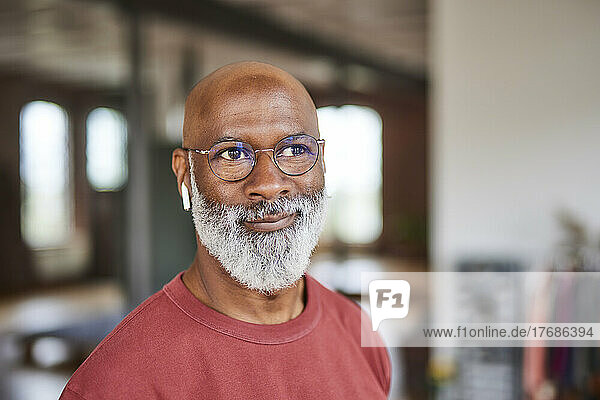 Smiling bald man with grey beard wearing eyeglasses at home