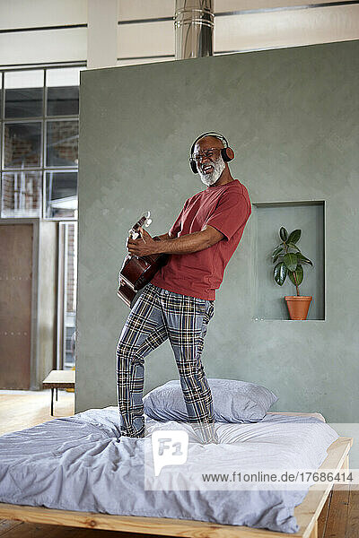 Reifer Mann mit Kopfhörern  der zu Hause im Bett Gitarre spielt