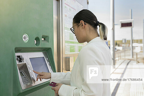 Young businesswoman holding credit card buying ticket at tram station