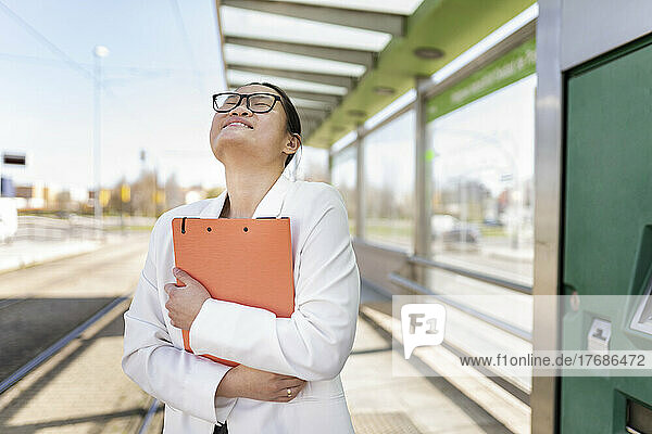 Happy businesswoman holding file folder standing at tram station