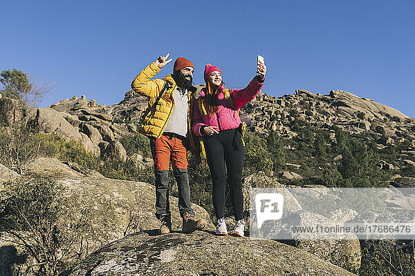 Smiling young woman talking with man gesturing peace sign standing on rock