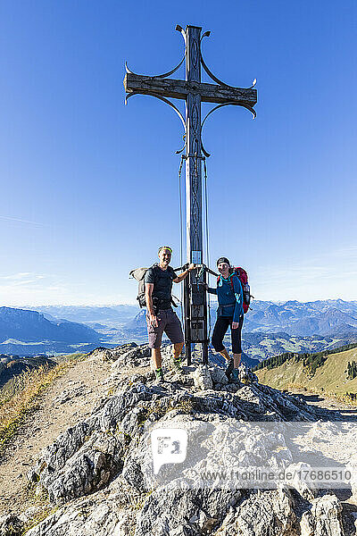 Germany  Bavaria  Two hikers posing in front of summit cross on Geigelstein mountain