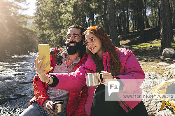 Young woman taking selfie with bearded man through smart phone on sunny day