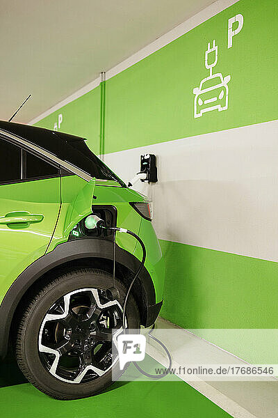 Green car being charged by wall at electric charging station