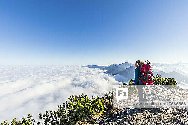 Germany  Bavaria  Female hiker standing on mountaintop admiring fog shrouded peaks of Bavarian Prealps