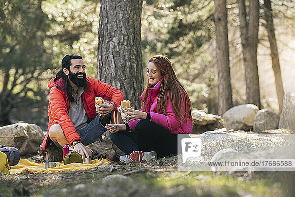 Cheerful man and woman with food sitting in forest