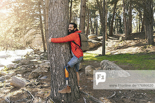 Happy disabled man hugging tree in forest