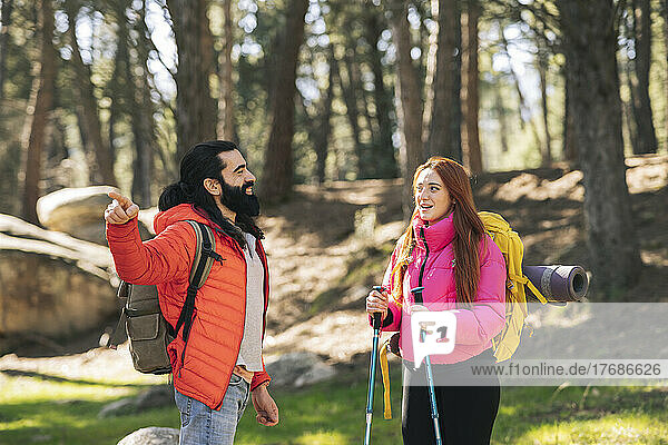Young woman talking with boyfriend wearing backpack pointing in forest