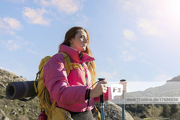 Young woman wearing backpack standing with hiking poles on sunny day