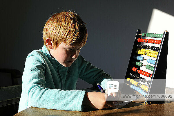 Junge macht Hausaufgaben mit Abakus auf dem Tisch zu Hause