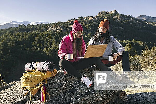 Junge Frau teilt Laptop mit Freund  der auf einem Felsen sitzt
