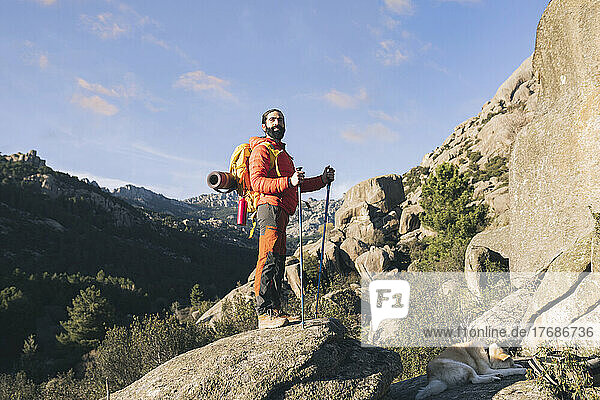 Man wearing backpack standing with hiking poles on rock