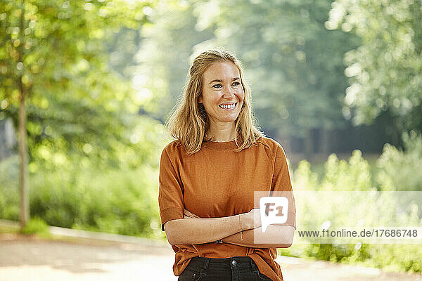 Smiling blond woman with arms crossed standing in park