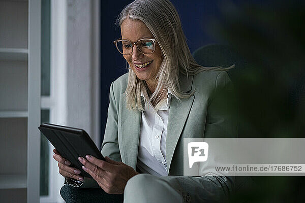 Happy businesswoman with tablet PC sitting on chair