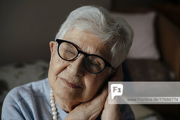 Senior woman leaning head on hands with eyes closed at home