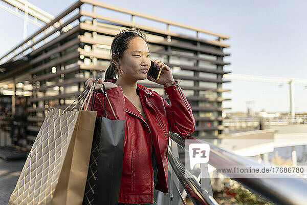 Junge Frau mit Einkaufstasche telefoniert am Geländer
