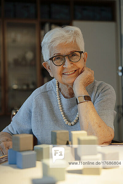 Glückliche ältere Frau mit Spielzeugklötzen  die zu Hause am Tisch sitzt