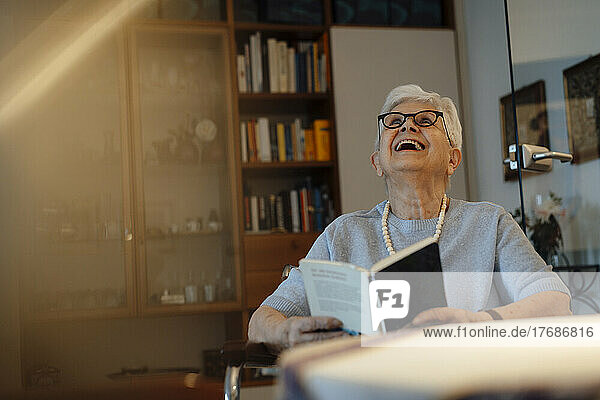 Glückliche ältere Frau mit Buch  die zu Hause sitzt