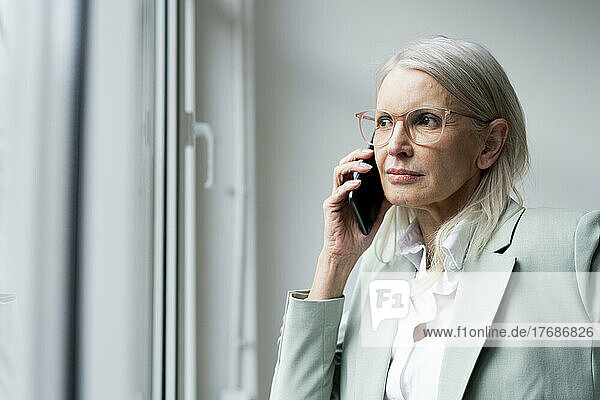 Businesswoman looking out of window talking on smart phone at office