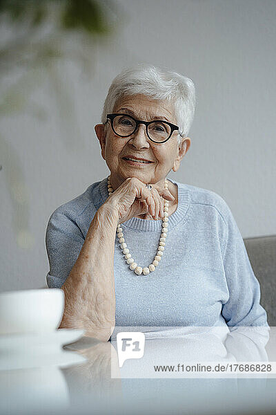 Happy senior woman with hand on chin sitting at table