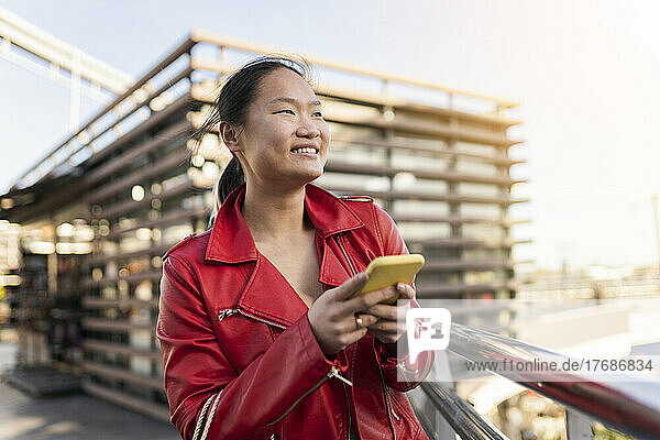 Lächelnde Frau hält Smartphone am Geländer