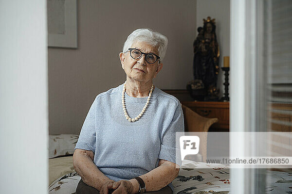 Lonely senior woman sitting on bed in bedroom at home