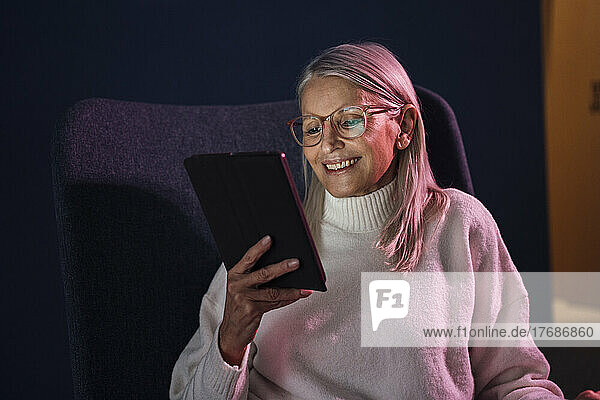 Smiling senior woman watching tablet PC sitting on chair