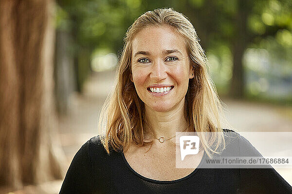 Smiling woman with blond hair standing in park