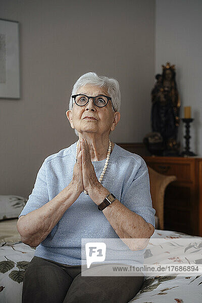 Senior woman with hands clasped sitting on bed at home