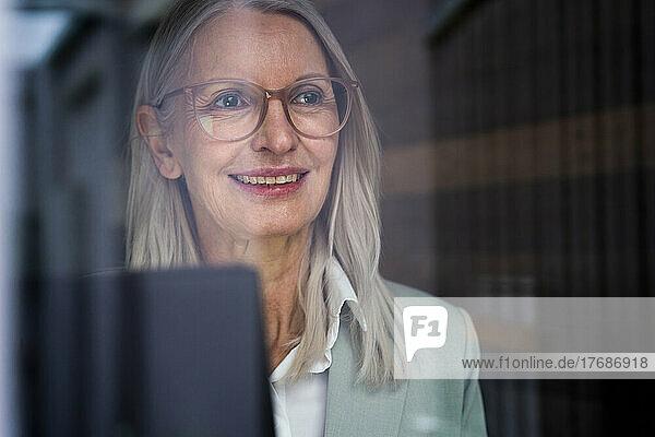 Thoughtful businesswoman with eyeglasses seen through glass
