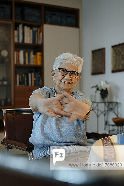 Smiling woman stretching hands sitting on chair at home