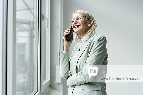Senior businesswoman talking on smart phone near window at office