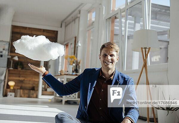 Happy businessman with levitating cloud network sitting in office