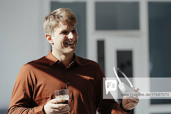 Happy businessman holding glass and virtual reality simulator in office