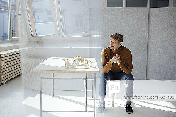 Happy architect with hands clasped sitting by desk in office